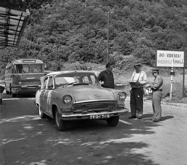 A motorist presenting documents to officers at a Cold War frontier