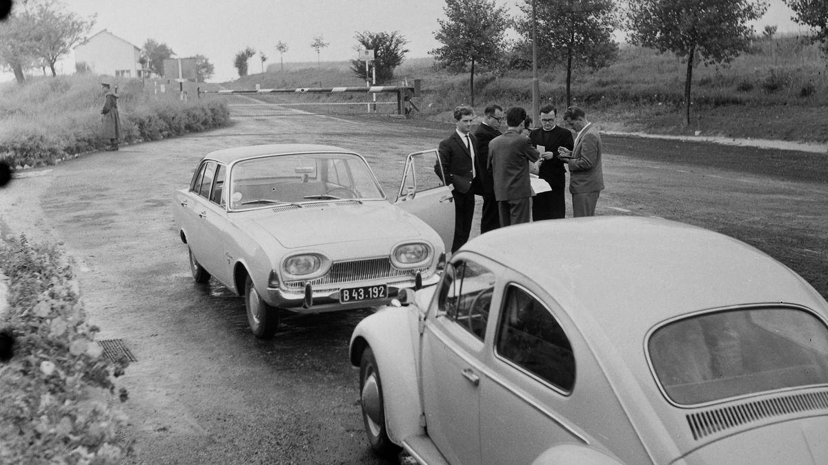 Travellers and officials gathered beside cars at a Cold War border barrier