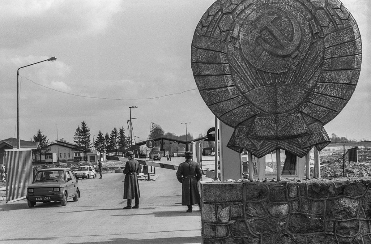 Cold War road checkpoint marked with a Soviet state emblem and uniformed guards
