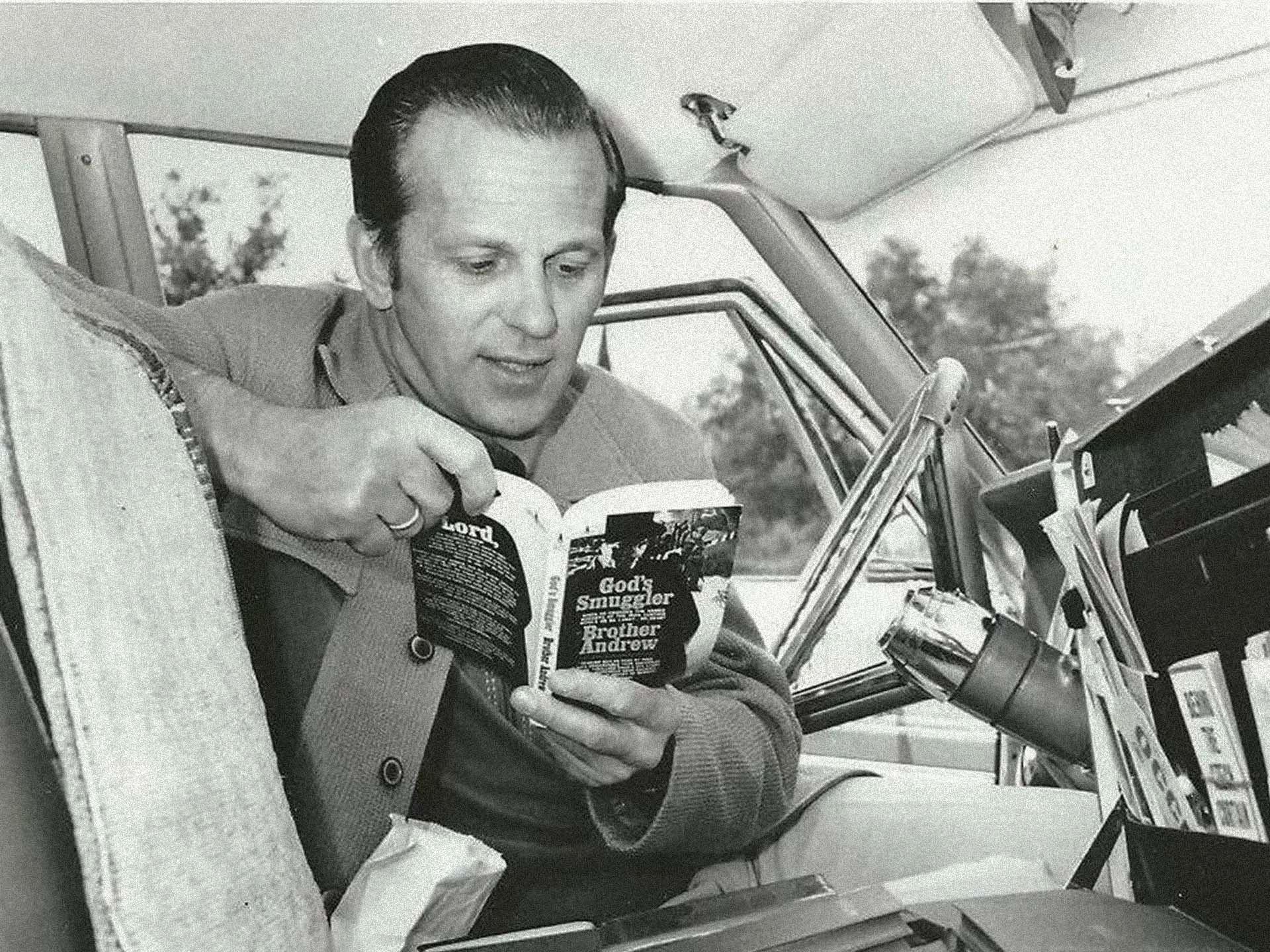 Brother Andrew seated in a car holding a copy of God's Smuggler